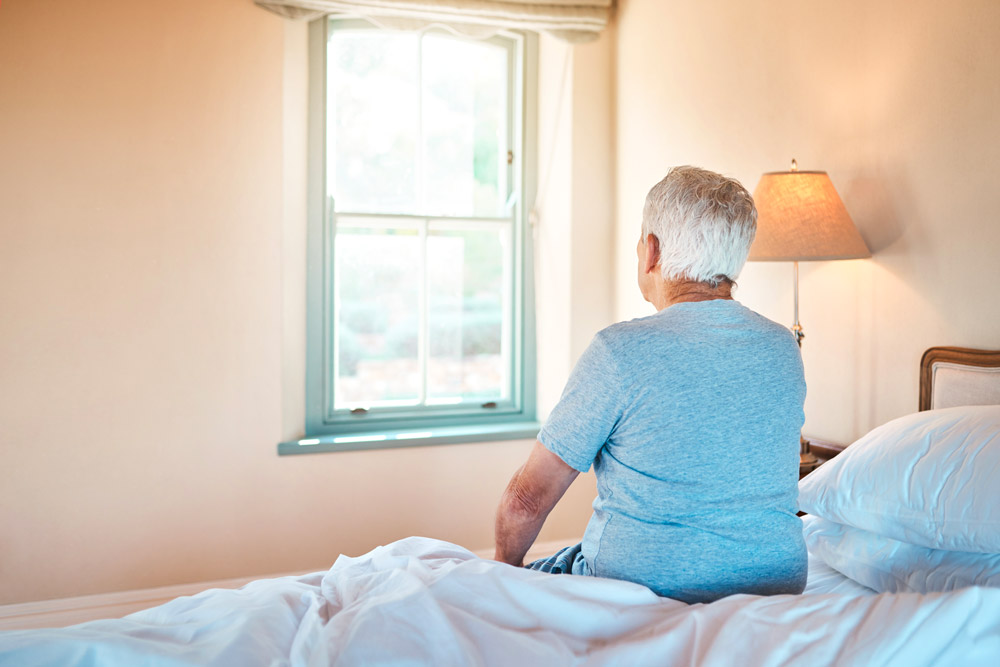 Homme assit sur un lit qui regarde par la fenêtre