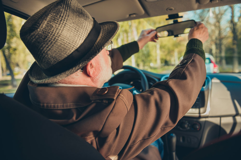 Homme ainée au volant d'une voiture qui ajuste son rétroviseur